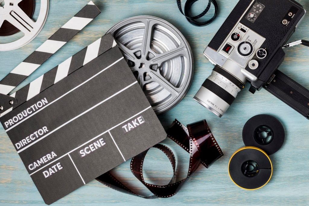 an-elevated-view-of-clapperboard-film-reels-film-strips-and-camcorder-on-blue-wooden-backdrop-scaled