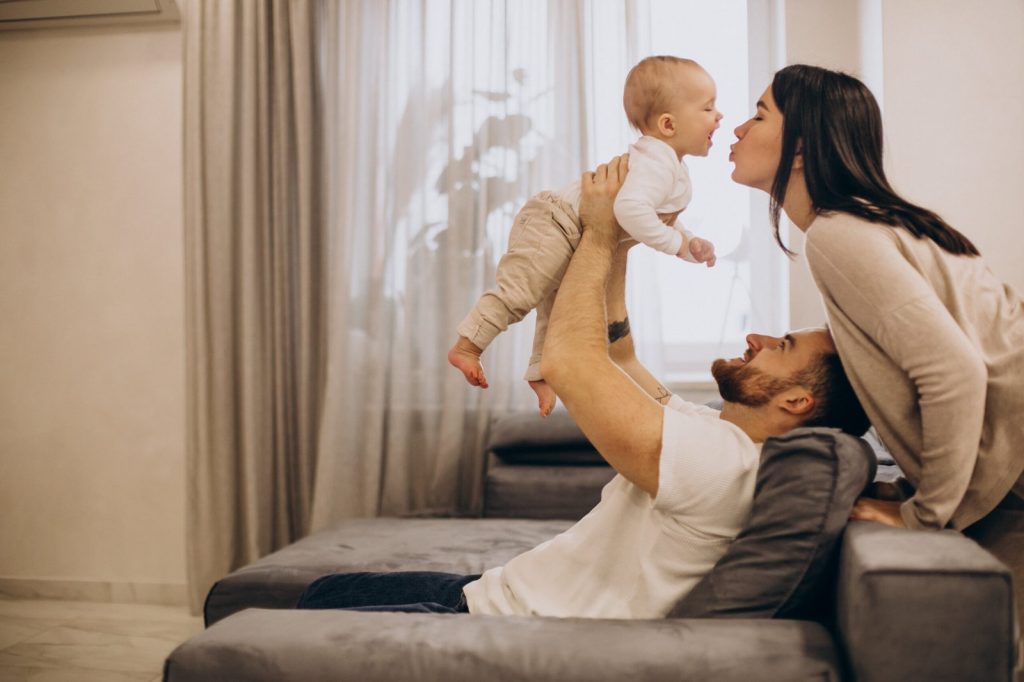young-family-with-toddler-baby-daughter-sitting-on-coach-at-home-scaled