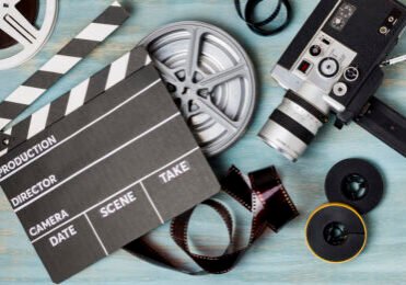 an-elevated-view-of-clapperboard-film-reels-film-strips-and-camcorder-on-blue-wooden-backdrop